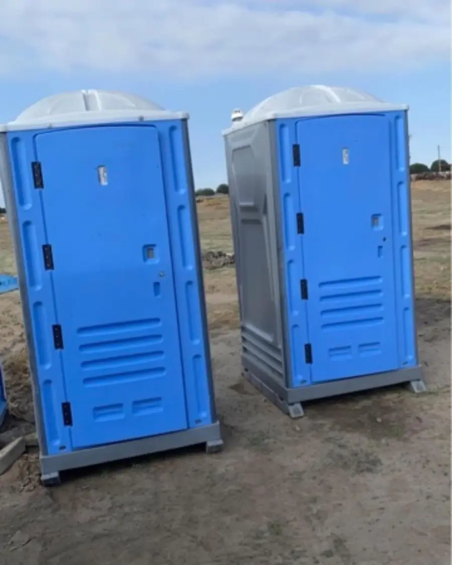 Two portable toilets on dry ground at a sunny job site