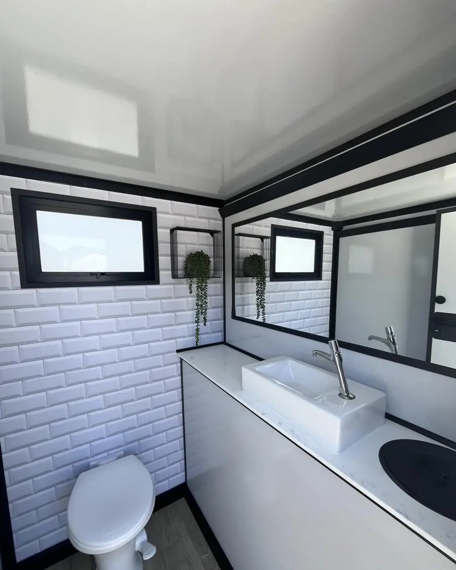 Restroom trailer interior with vanity sink, mirror, plant and white tile walls